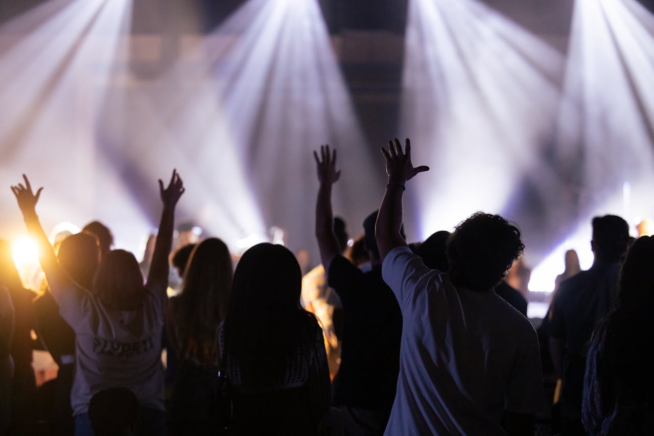 Silhouette of a crowd with raised hands enjoying a worship concert with bright stage lights.
